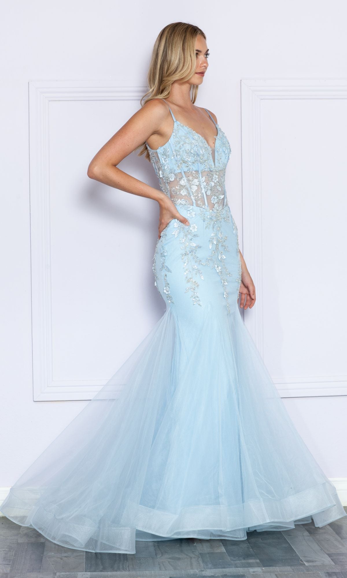 A woman stands sideways wearing the Sheer-Corset-Bodice Long Mermaid Prom Dress 9374 in blue, featuring a sleeveless design, sheer panels, and delicate floral embroidery.
